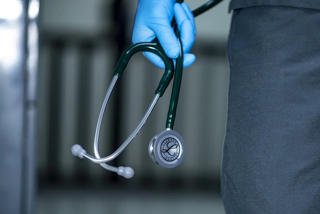 A gloved clinician holding a stethoscope in a hospital corridor